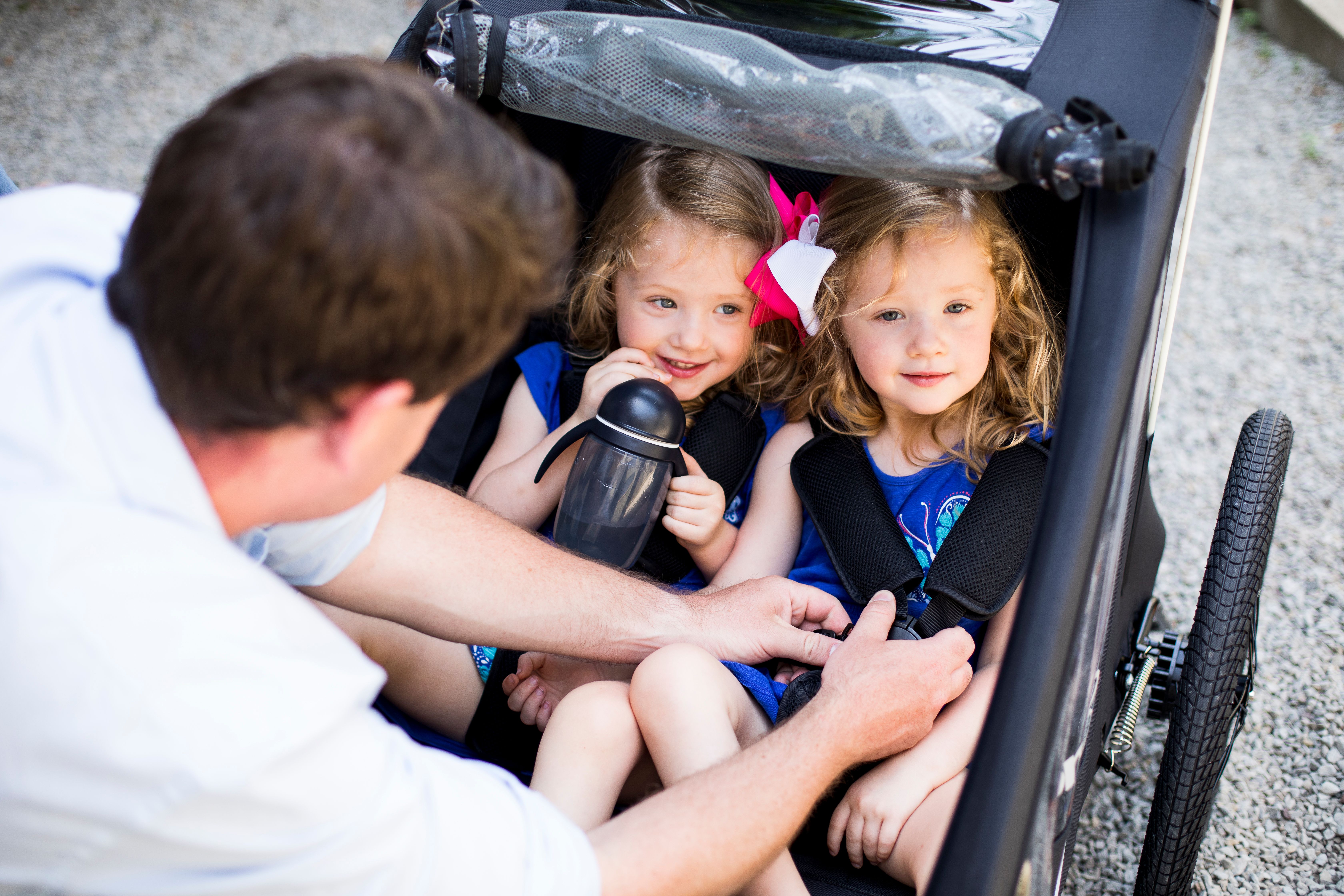 Two children in CocoonX2 while dad buckles them in